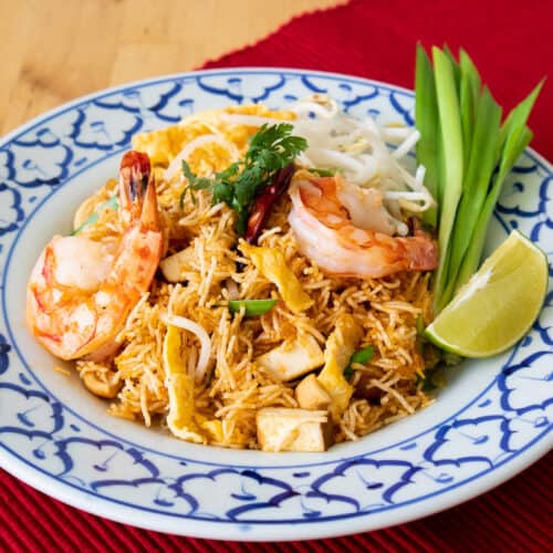 A plate of crispy noodles with shrimp, garlic chives, and a wedge of lime.