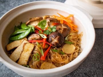 Glass noodles in clay pot topped with tofu, mushrooms, sugar snap peas, red pepper and carrots