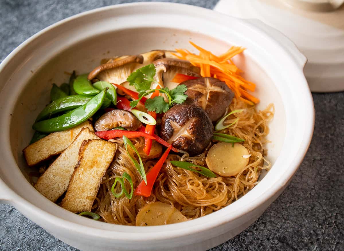 Glass noodles in clay pot topped with tofu, mushrooms, sugar snap peas, red pepper and carrots