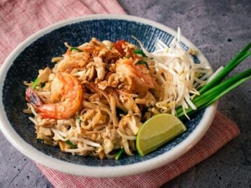 A plate of pad thai shrimp with lime and beansprouts and garlic chives on the side