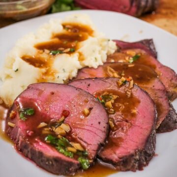 A plate of slices of roast beef with Thai gravy on it and a side of mashed potatoes
