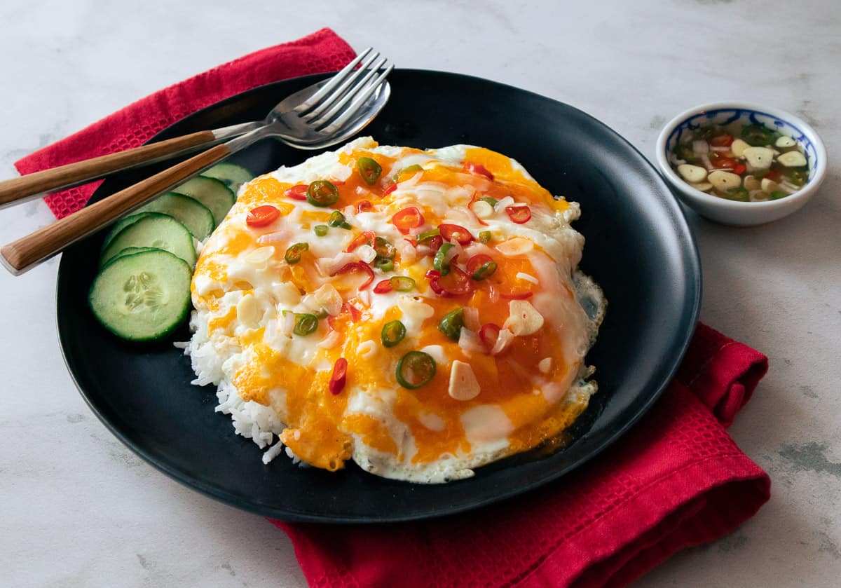 a plate of marble eggs on rice with red and green chilies on top and cucumber on the side