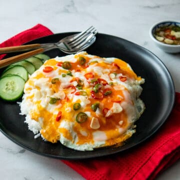 a plate of marble eggs on rice with red and green chilies on top and cucumber on the side