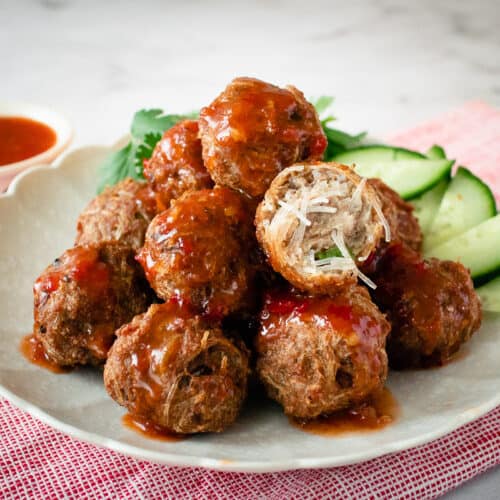 A plate of noodle meatballs with sweet chili sauce, with one meatball cut open