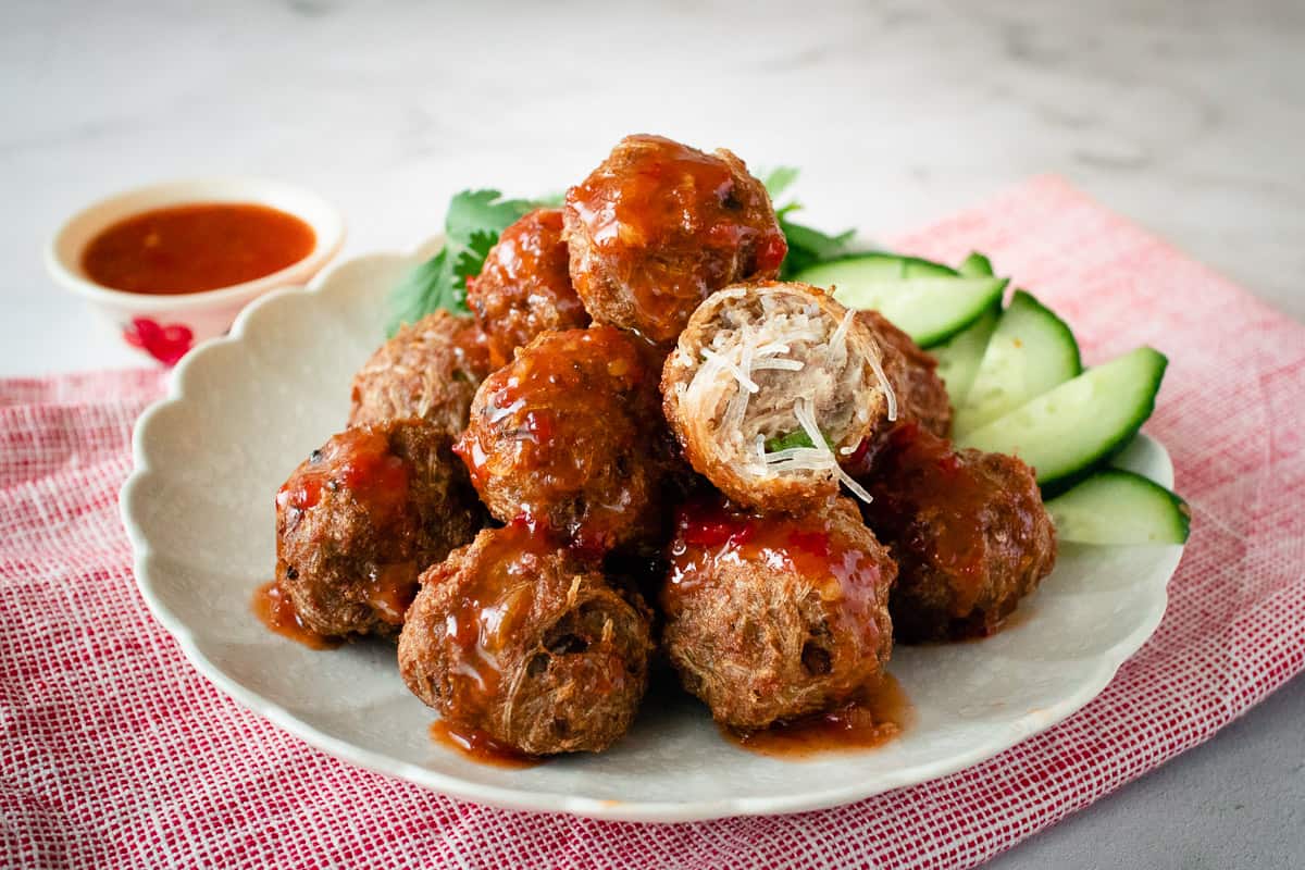 A plate of noodle meatballs with sweet chili sauce, with one meatball cut open