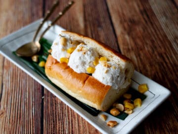 3 scoops of coconut ice cream in a hotdog bun, topped with peanuts and corn.