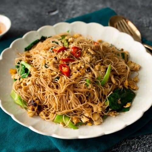 A plate of pad see ew with rice vermicelli with a side of chili vinegar