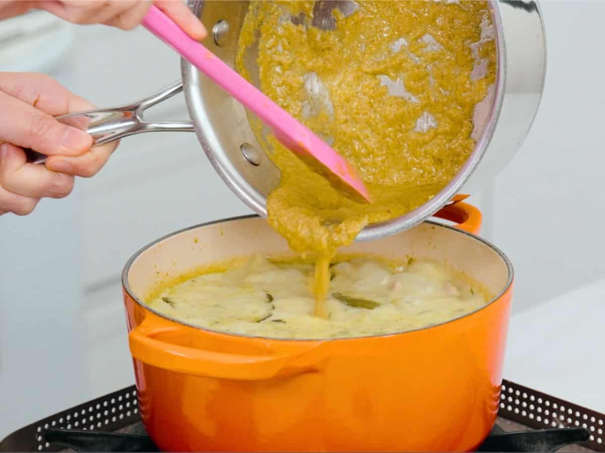 additional curry paste being added to a pot of green curry.
