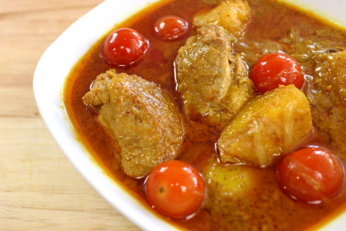 A bowl of yellow curry chicken with tomatoes and potato