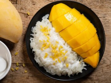 a plate of mango and sticky rice with mung beans on top of the rice