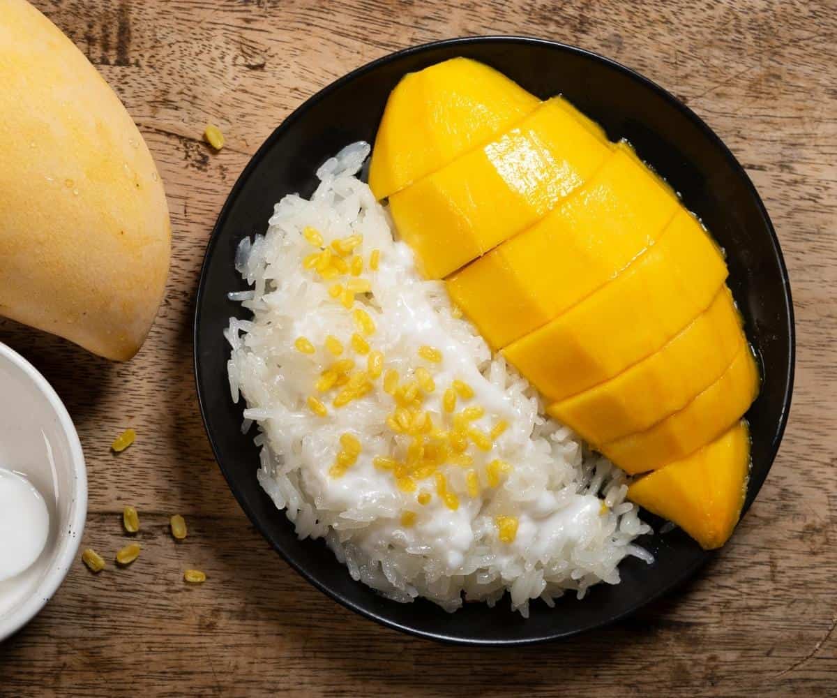 a plate of mango and sticky rice with mung beans on top of the rice