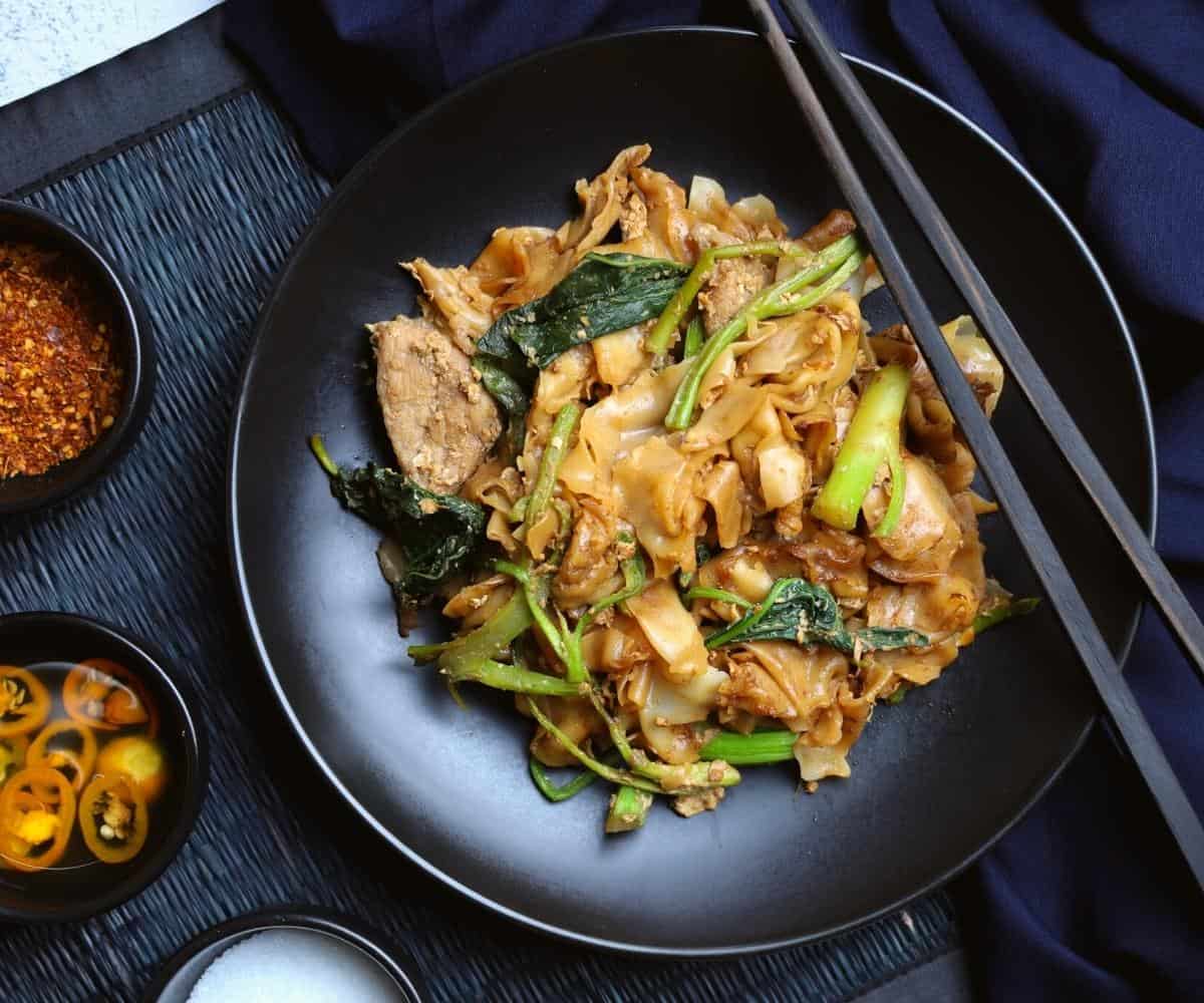 Pad see ew in a black bowl with chopsticks on top