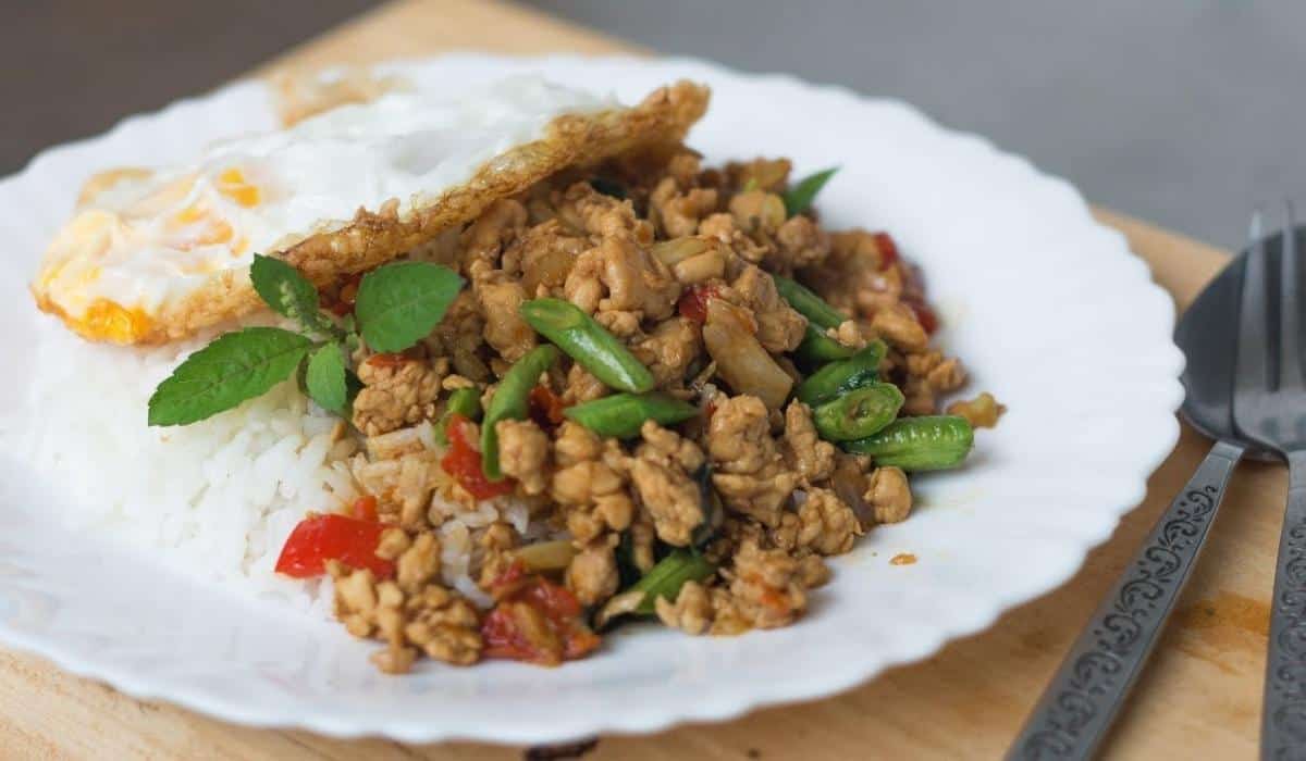 a plate of rice with basil chicken stir fry on top and a fried egg.