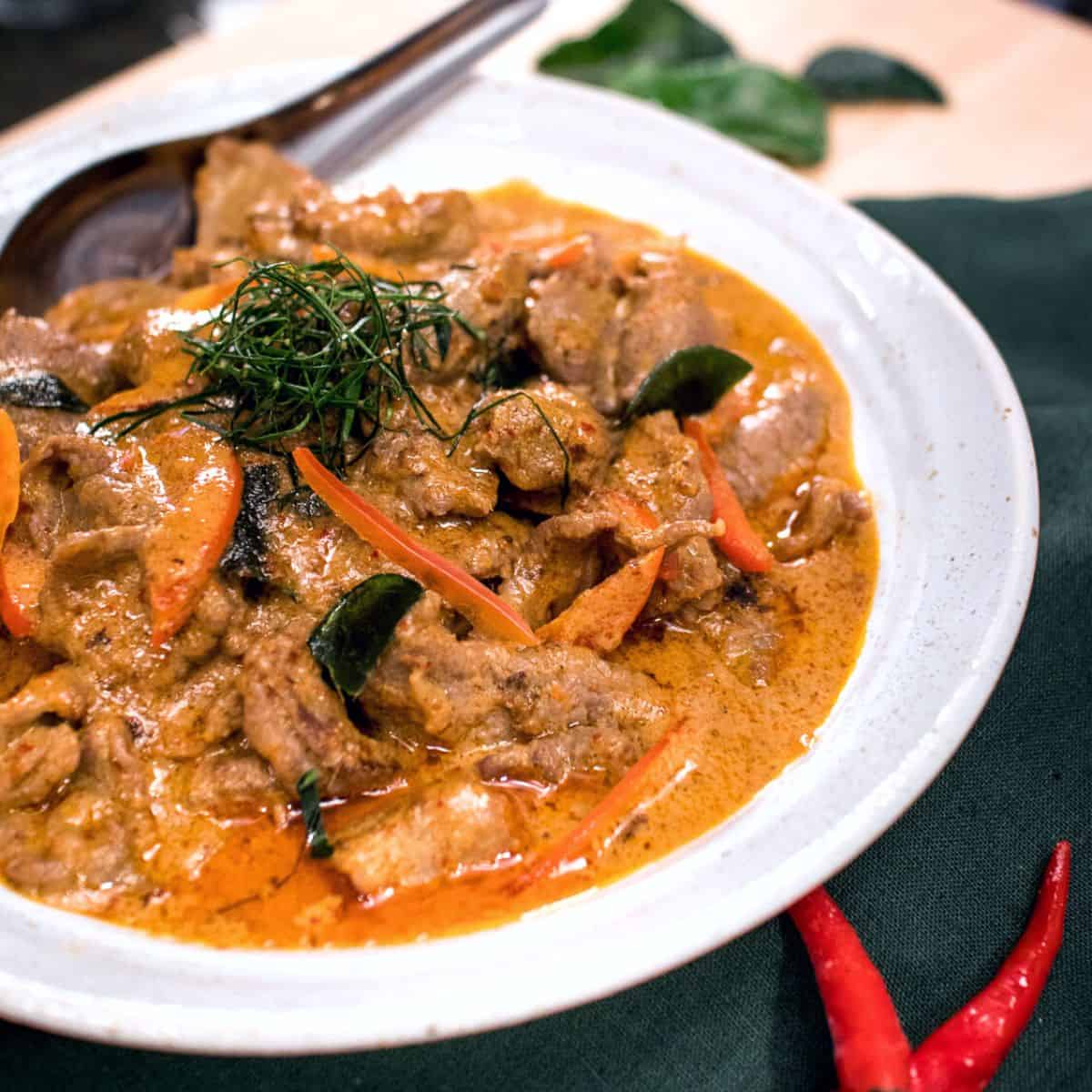 a bowl of panang beef curry with kaffir lime leaves on top