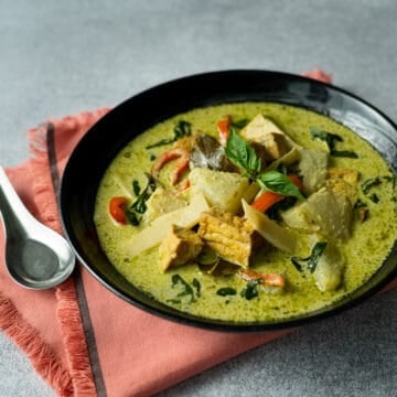 a black bowl of vegan green curry on an orange napkin
