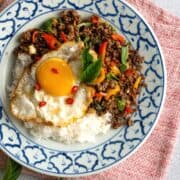 a plate of pad kra pao beef on rice with a fried egg on top. With a bowl of fish sauce condiment on the side. Text overlay "Thai Basil Stir Fry Pad Kra Pao"