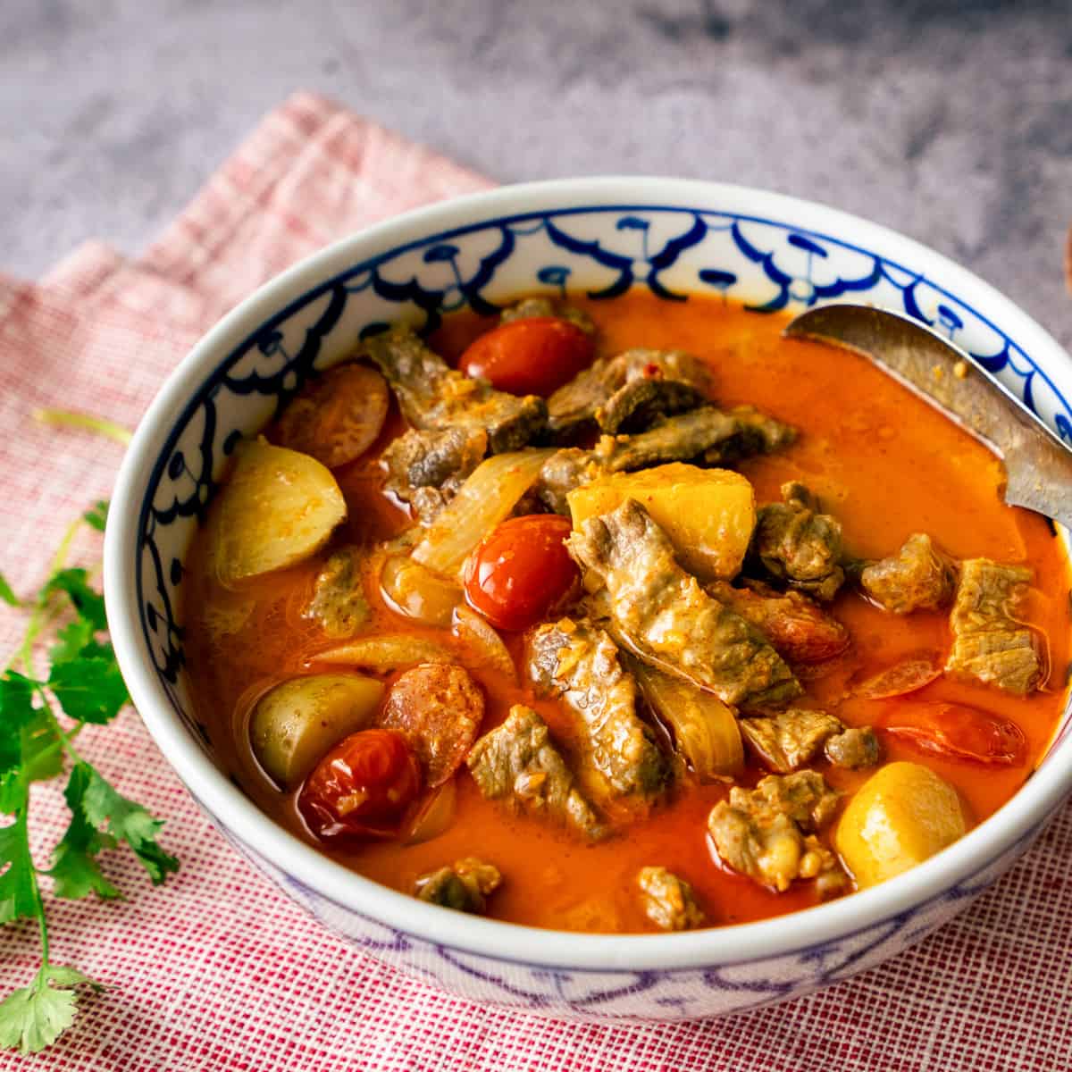 A bowl of yellow curry beef with a cilantro sprig on the side