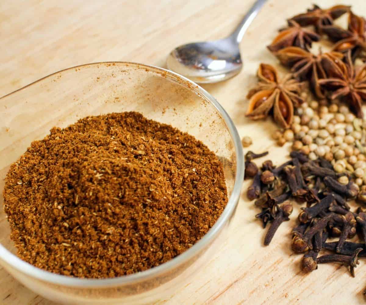 a bowl of five spice powder with cloves, coriander seeds and star anise in the background.