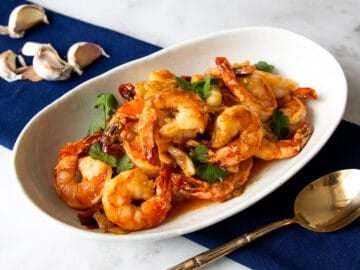 A plate of garlic shrimp with a spoon on the side