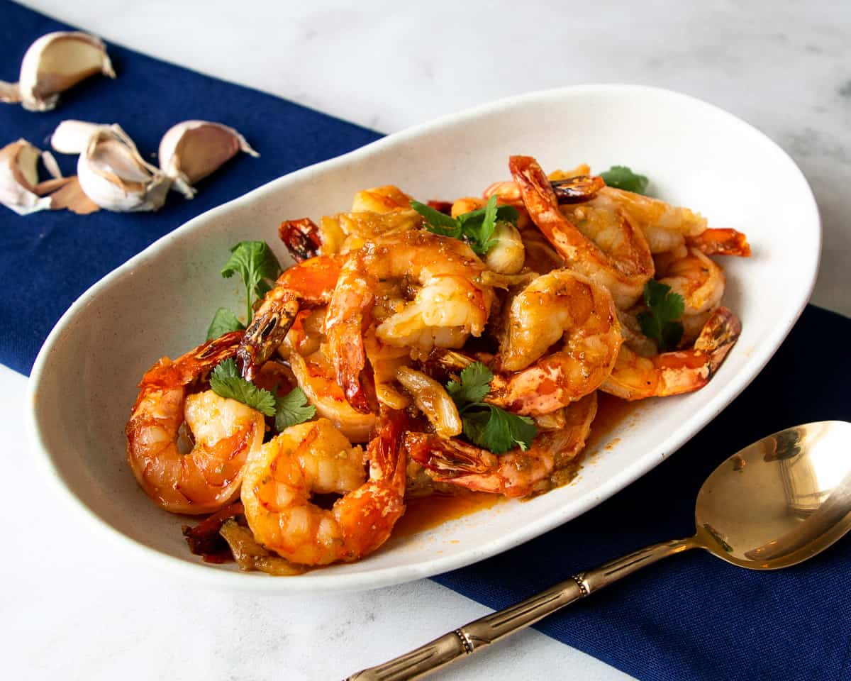 A plate of garlic shrimp with a spoon on the side