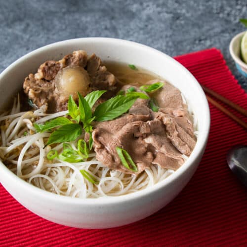 a bowl of oxtail beef pho with a lime wedge and thai basil on the side