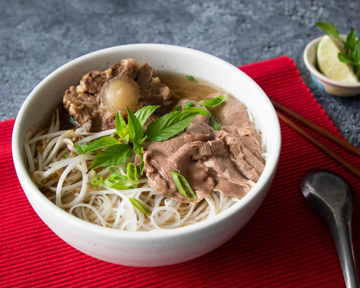 a bowl of oxtail beef pho with a lime wedge and thai basil on the side