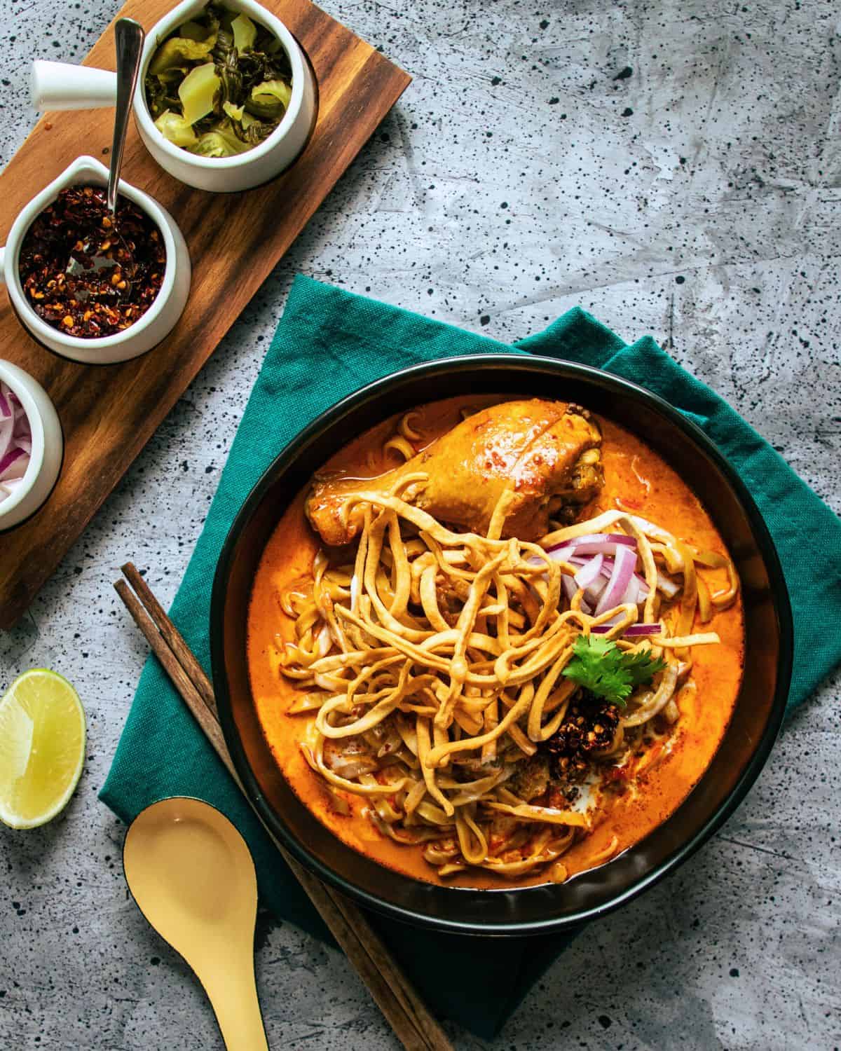 a bowl of khao soi with chicken drumsticks with condiments on the side.