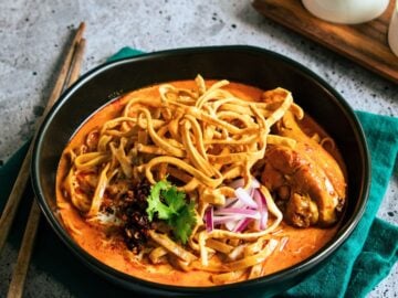 a bowl of khao soi with chicken drumsticks with condiments on the side.