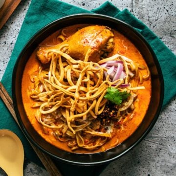 a bowl of khao soi with chicken drumsticks with condiments on the side.