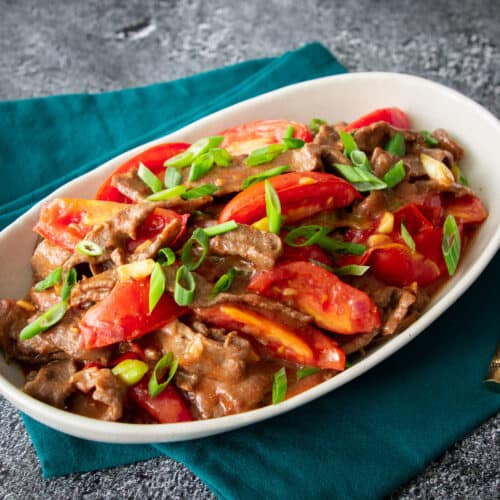 a plate of tomato beef stir fry with green onions on top