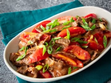 tomato beef stir fry on an oval plate on green napkin.