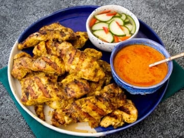 A plate of chicken satay with a bowl peanut sauce and a bowl cucumber pickle.