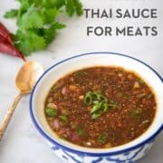 A bowl of nam jim jeaw sauce with cilantro, cilies and spoon in the background. Text overlay "the best Thai sauce for meats" and hotthaikitchen.com