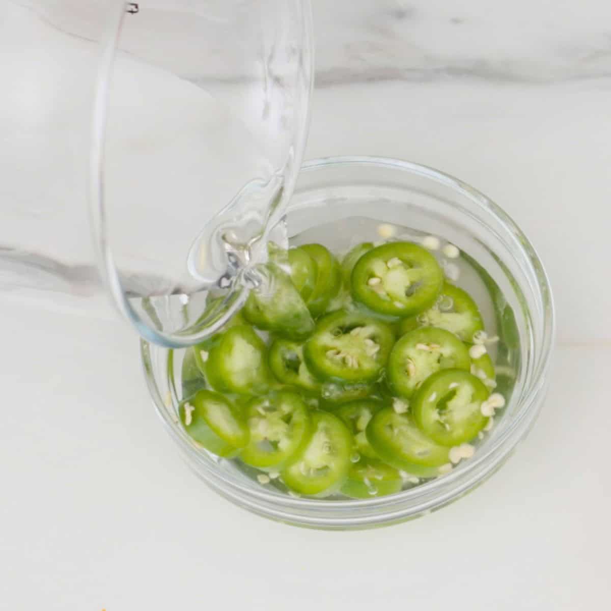 a bowl of sliced serrano chilies with vinegar being poured into it.