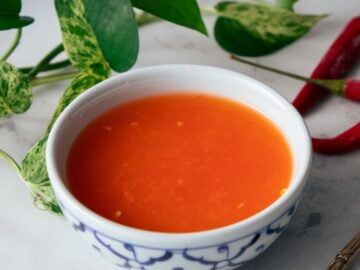 a bowl of chili vinegar with chilies and plants in the background.