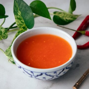 a bowl of chili vinegar with chilies and plants in the background.