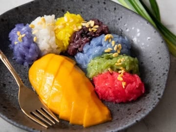 a plate of mango with 7 colours of sticky rice with mung beans on top.