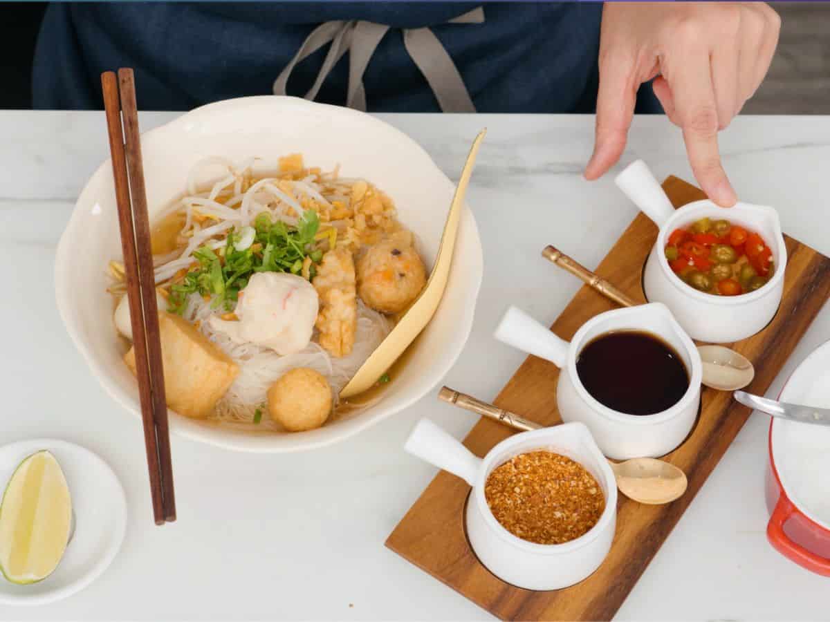 a bowl of noodle soup with condiments on the side