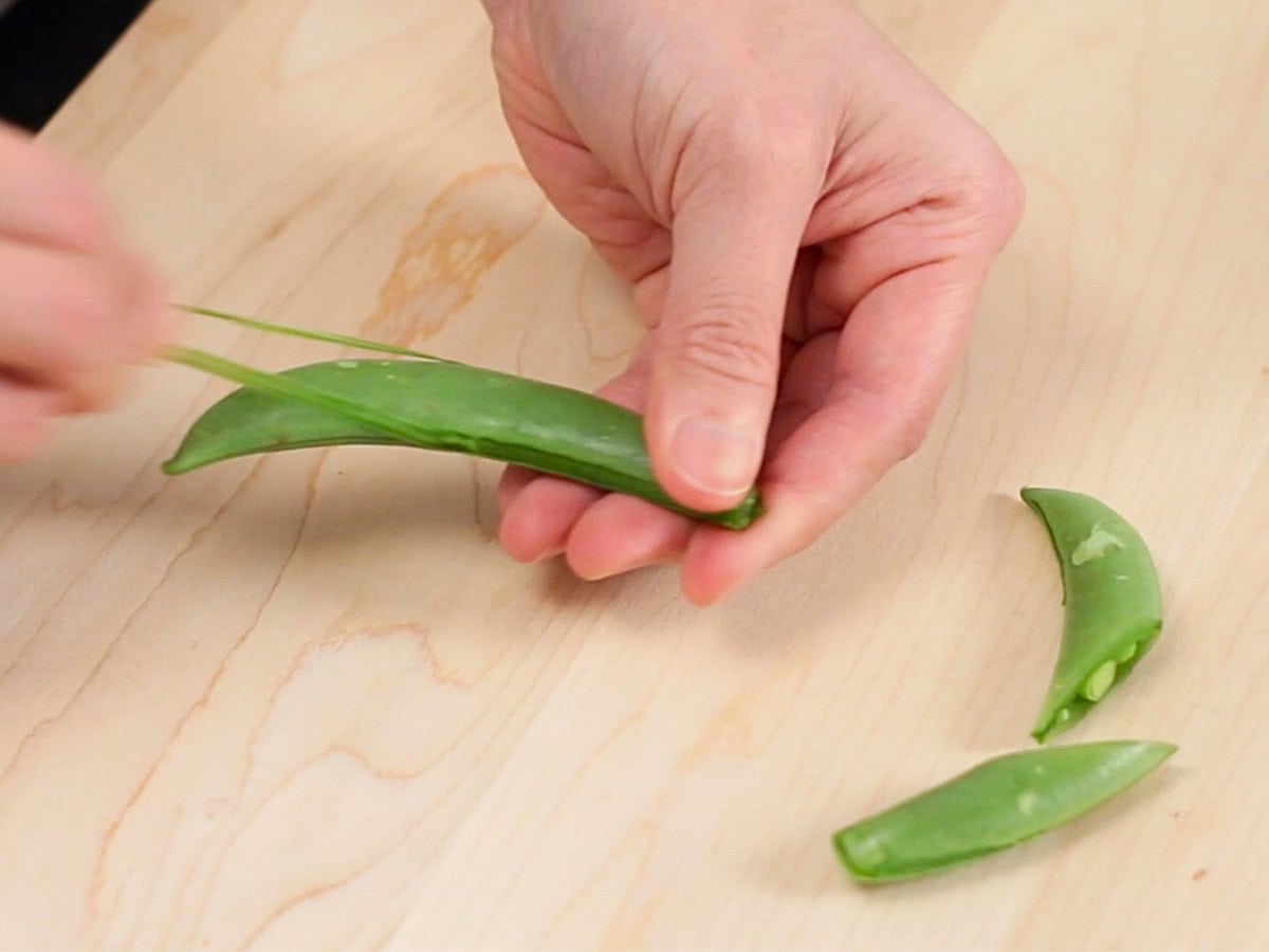 strings being removed from snap peas, and one snap pea cut in half on the table