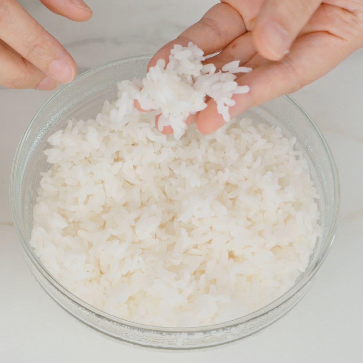 a bowl of sushi rice being picked up by fingers