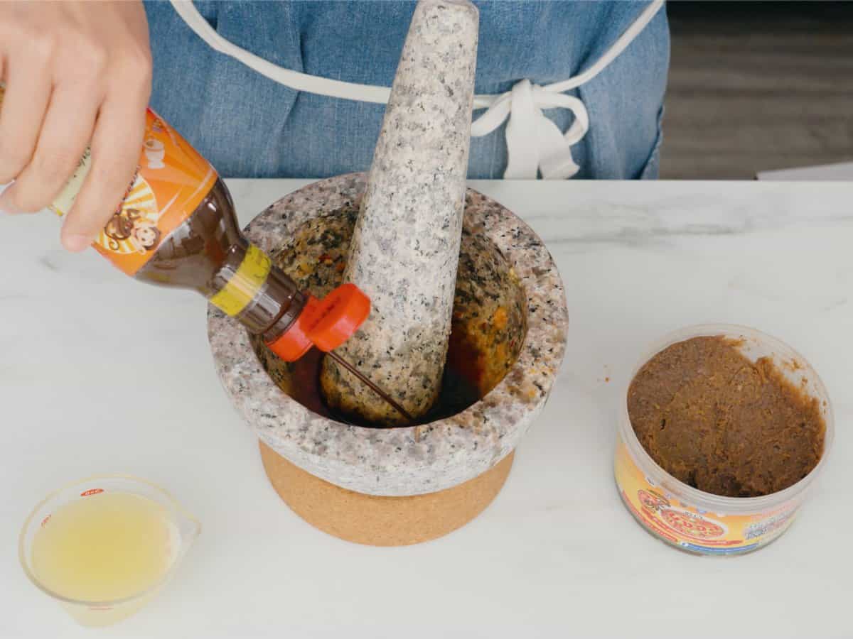 pla ra being squirted into a mortar with a tub of open shrimp paste on the side.