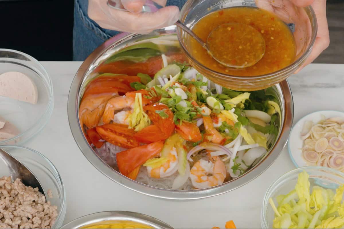 a thai salad being composed in a mixing bowl