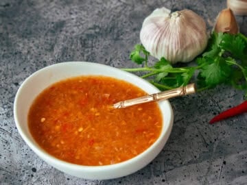 a bowl of Thai salad dressing with a spoon in it, with garlic cilantro and chilies in the background.