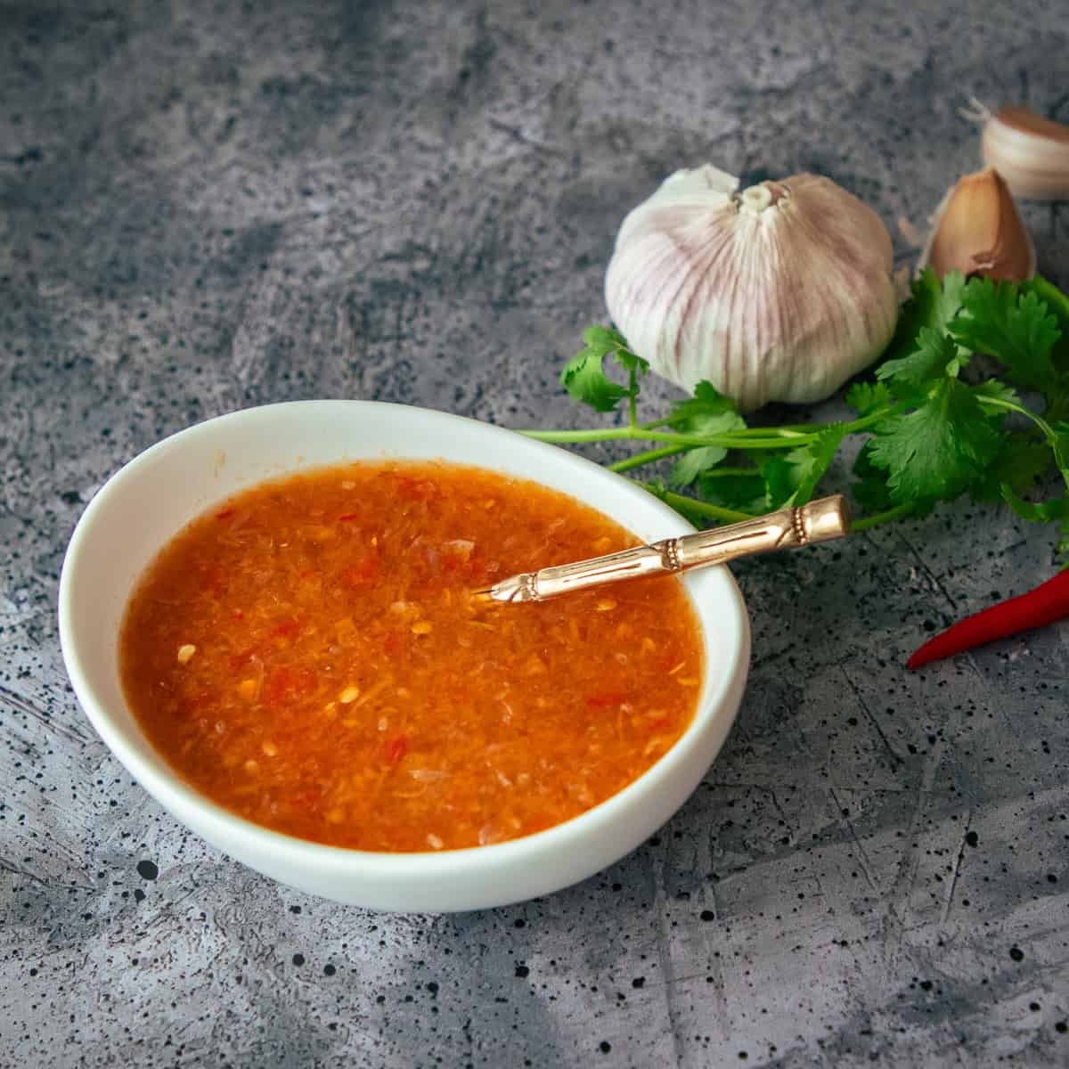 a bowl of Thai salad dressing with a spoon in it, with garlic cilantro and chilies in the background.