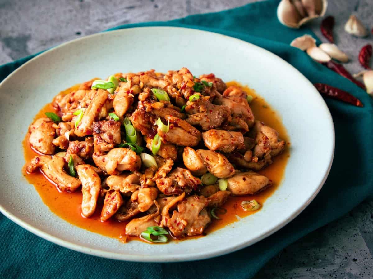 a plate for chili garlic chicken with dried chilies and garlic in the background.