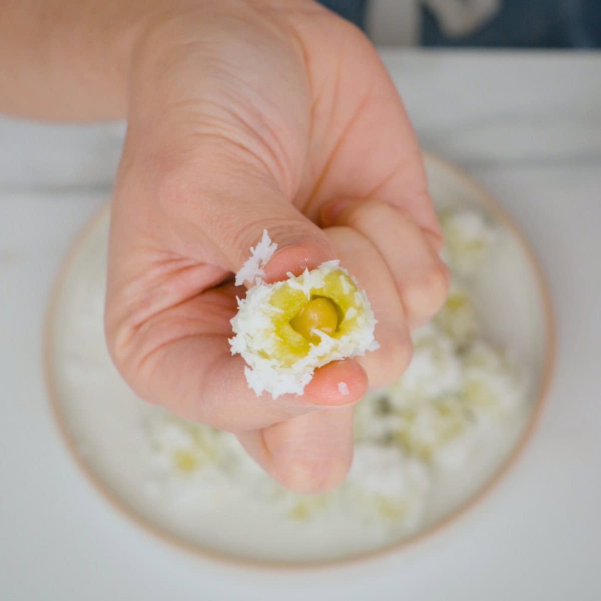 A hand holding up one piece of kanom ko cut open to show the palm sugar filling inside.